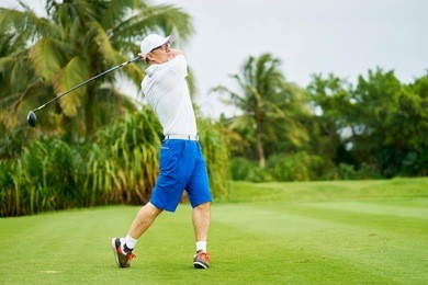asian man swinging club in golf course in summer