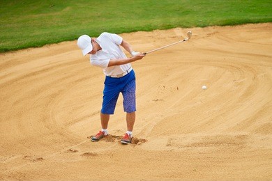 asian player swinging club in bunker of a course