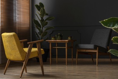 elegant and dark apartment interior with classic wooden furniture and a large potted plant next to blinds and a black wall with molding