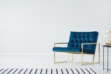 a minimalist living room interior with a white, empty wall, elegant, royal blue armchair with a metal, golden frame and a striped rug