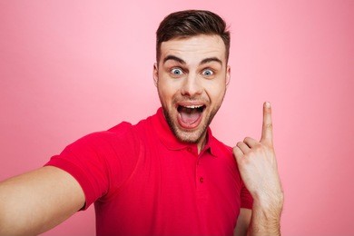 portrait of a happy young man pointing finger up while taking a