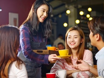 young smiling asian waitress serving coffee to customers.