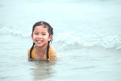 happy asian little child girl having fun to play water in the sea in summer vacation