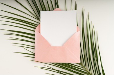 minimal composition with a pink envelope, white blank card and a palm leaf on a white background. mockup with envelope and blank card. flat lay. top view.