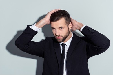 stunning, perfect, manly, virile, harsh guy in classic outfit holding two hands on head, looking to the side with serious expression, isolated on grey background