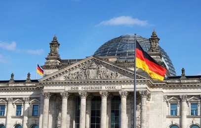 german flag waving at bundestag building in berlin germany front facade view in a sunny day with blue sky.