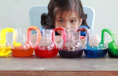 fun and easy science.5 years old asian girl making walking water experiment.food color add to the water in the recycled bottle,water moving along the paper then color mixed.concept of science for kid 