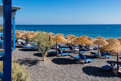 beach with umbrellas and deck chairs in santorini