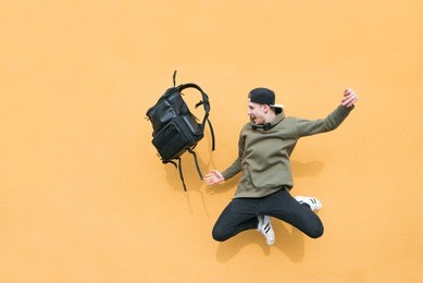 street young man jumping with a backpack on the background of an orange wall