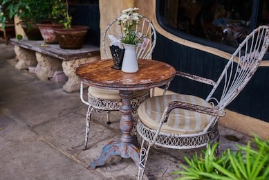 old white antique wrought iron furniture, shabby chic exterior. set of round table with flowers and two elegant chairs in the street in the old town. table on cafe background. vintage style.  

