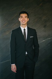portrait of a young chinese professional (lawyer, business man) in a suit standing against a dark stone background. 