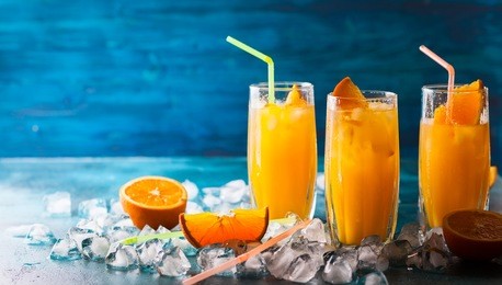 fresh orange juice in glasses, cubes of ice and slice of fruits  on blue table. healthy vitamin drink.