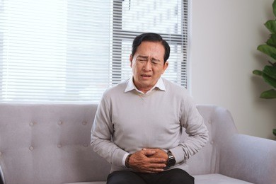 senior asian man with stomach ache while sitting on sofa