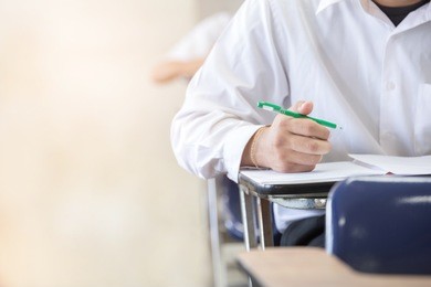 soft focus.high school or university student holding pencil writing on paper answer sheet.sitting on lecture chair taking final exam attending in examination room or classroom.student in uniform