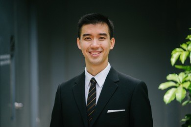 portrait of a young, chinese asian man in a suit. he is smiling at the camera. 
