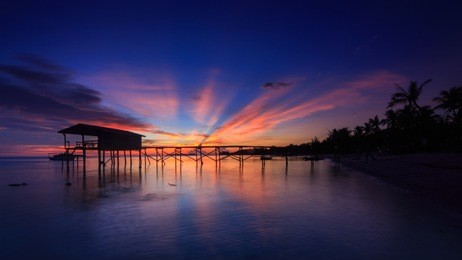 amazing beautiful sunset with silhouette wooden jetty and coconut tree at mantanani island, sabah, borneo. mantanani island has long stretch of white sandy beaches and crystal clear water.