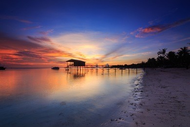 amazing beautiful sunset with silhouette wooden jetty and coconut tree at mantanani island, sabah, borneo. mantanani island has long stretch of white sandy beaches and crystal clear water.