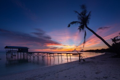 amazing beautiful sunset with silhouette wooden jetty and coconut tree at mantanani island, sabah, borneo. mantanani island has long stretch of white sandy beaches and crystal clear water.
