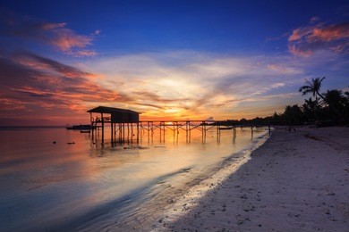 amazing beautiful sunset with silhouette wooden jetty and coconut tree at mantanani island, sabah, borneo. mantanani island has long stretch of white sandy beaches and crystal clear water.