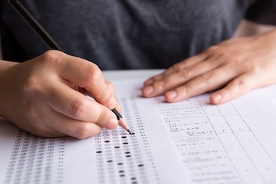 students hand holding pencil writing selected choice on answer sheets and mathematics question sheets. students testing doing examination. school exam 