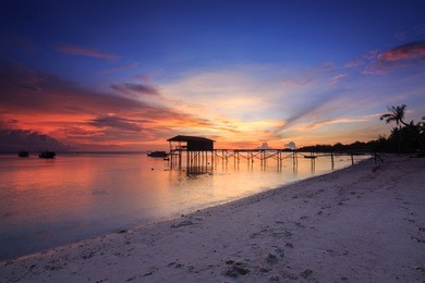 amazing beautiful sunset with silhouette wooden jetty and coconut tree at mantanani island, sabah, borneo. mantanani island has long stretch of white sandy beaches and crystal clear water.
