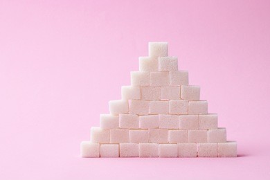 
a handful of sugar cubes on a pastel background. the sugar pyramid. minimalism, design, diabetes, sweets, calories. 