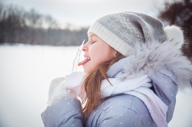 a girl playing with snow in winter, making snow angel and eating icicles 