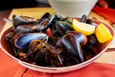 florence, tuscany / italy. - april 15, 2018. italian cuisine seafood: mussels with herbs and lemon, served in a ceramic plate on an orange tablecloth, next fork.