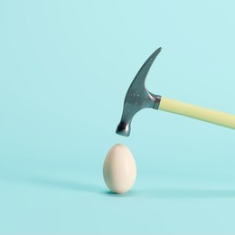 hammer is hitting on an egg with blue background. minimal idea creative concept.
