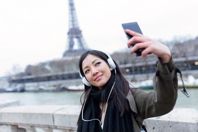 shot of pretty asian young woman taking a selfie in front of eiffel tower in paris while listening to music.