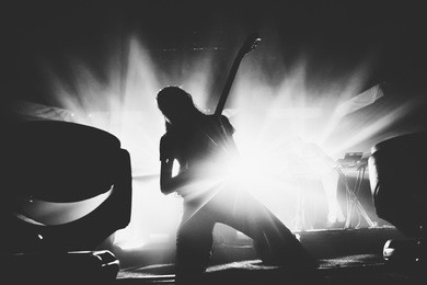 female guitarist silhouette playing guitar solo on a stage on a knees 