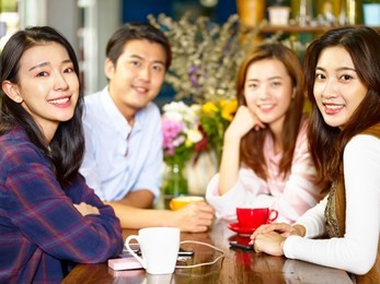 group of four happy asian young adults man and woman looking at camera smiling while gathering in coffee shop.