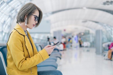 pretty asian woman using smartphone on the airport terminal while waiting for flight,technology and travel concept