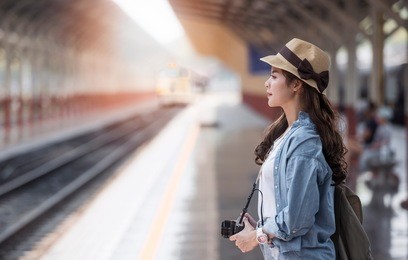 asian backpack traveler woman with camera standing   at train station platform and waiting train arrivel, summer holiday travelling or young tourist concept