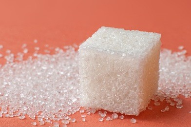 macro shot of a cube of sugar and sugar of sand behind it, on a colored surface
