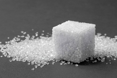 macro shot of a cube of sugar and sugar of sand behind it, on a colored surface