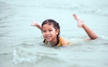happy asian little child girl having fun to play water in the sea in summer vacation