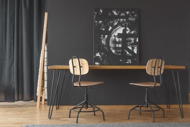 black and white painting standing against a dark wall, on a wooden dining table in monochromatic room interior