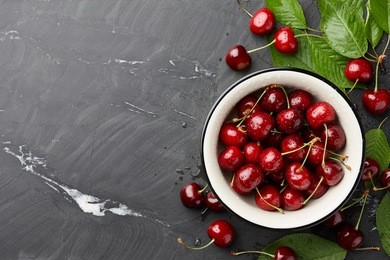 fresh sweet cherries bowl with leaves in water drops on stone background, top view