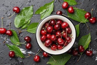 fresh sweet cherries bowl with leaves in water drops on stone background, top view