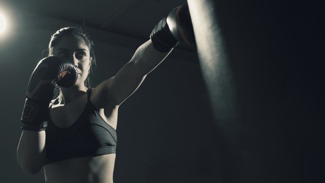 young woman doing boxing training at the gym, she is wearing boxing gloves and hitting the punching bag