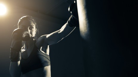 young woman doing boxing training at the gym, she is wearing boxing gloves and hitting the punching bag