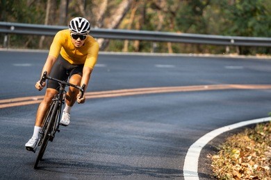 asian man in yellow cycling jersey riding on road bike with willful face.