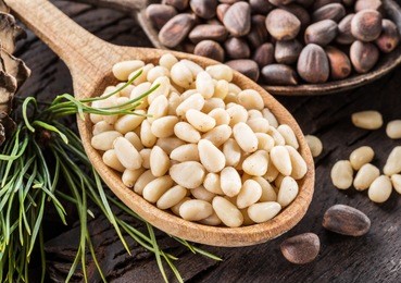 pine nuts in the spoon and pine nut cone on the wooden table. organic food.