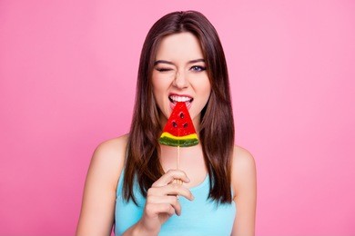 it's better to lick it! close up portrait of beautiful stylish trendy sexy attractive colorful funny joyful funky fancy girl wearing blue singlet biting lollipop on stick, isolated on pink background