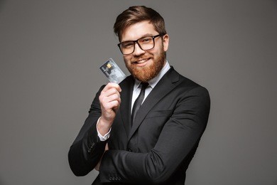 portrait of a happy young businessman holding credit card isolated over gray background