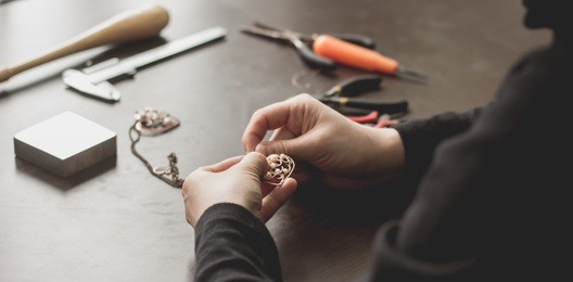 girl craftsman making copper wire wrapped jewelry heart pendant with pearls close up top view. female hands holding adornment jewelery handmade art product. accessories bijouterie