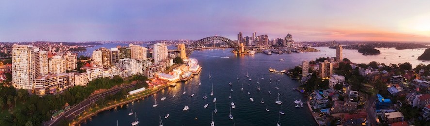 pink sunset over sydney city cbd landmarks around sydney harbour connected by the sydney harbour bridge in elevated aerial panorama from lavender bay and north sydney shores.