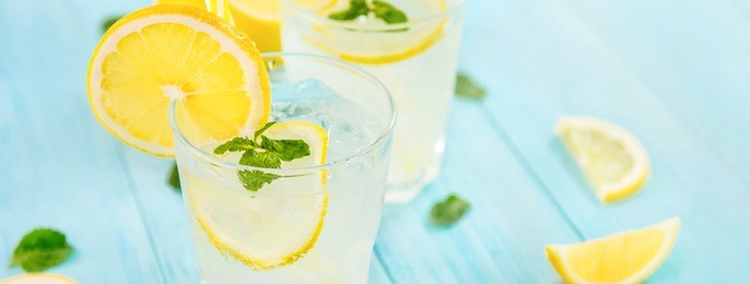 refreshing drinks for summer, cold sweet and sour lemonade juice with ice cubes in the glasses garnished with sliced fresh lemons, panoramic banner