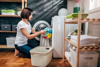 woman wearing white shirt taking clothes out washing machine at laundry room
